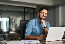 Mladý muž se usmívá při práci na notebooku v kanceláři