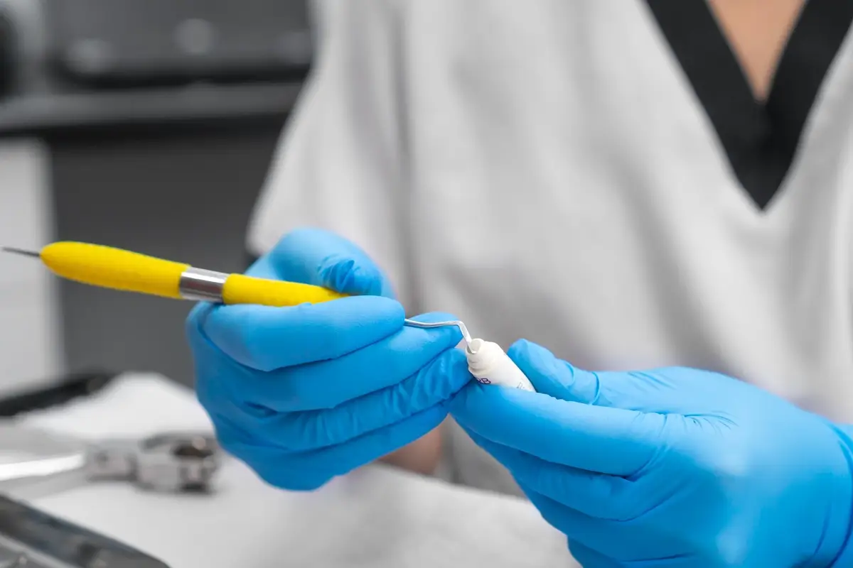 zuby 3 - SportDeník Zubař stojí a v rukavicích nabírá bílý amalgám do pomůcky dentistů, kterou jej nanáší do zubu
