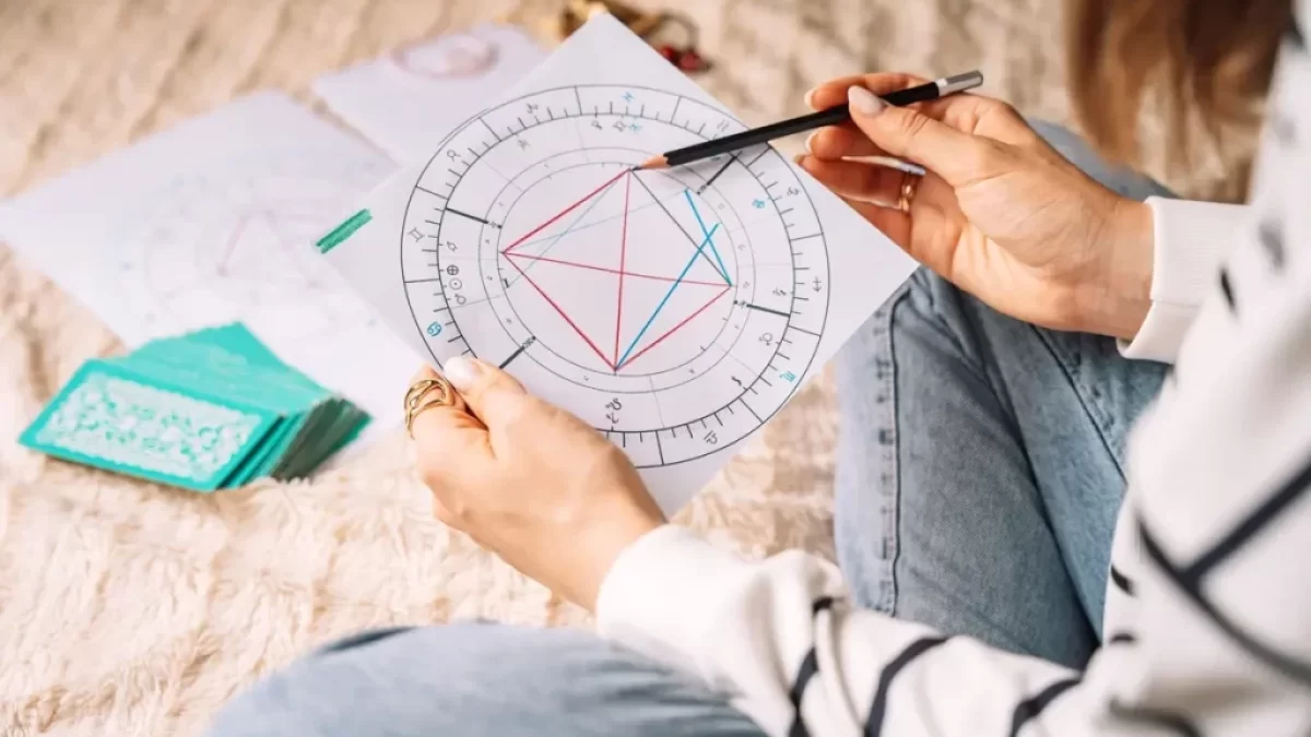 Mladá žena sedí na zemi a před sebou má horoskop, který zkoumá
