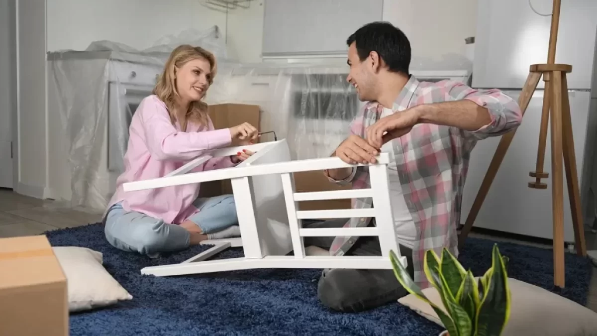 Mladý pár sedící na zemi skládá bílou židli ze švédského obchodního domu IKEA