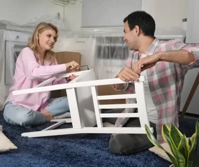 Mladý pár sedící na zemi skládá bílou židli ze švédského obchodního domu IKEA