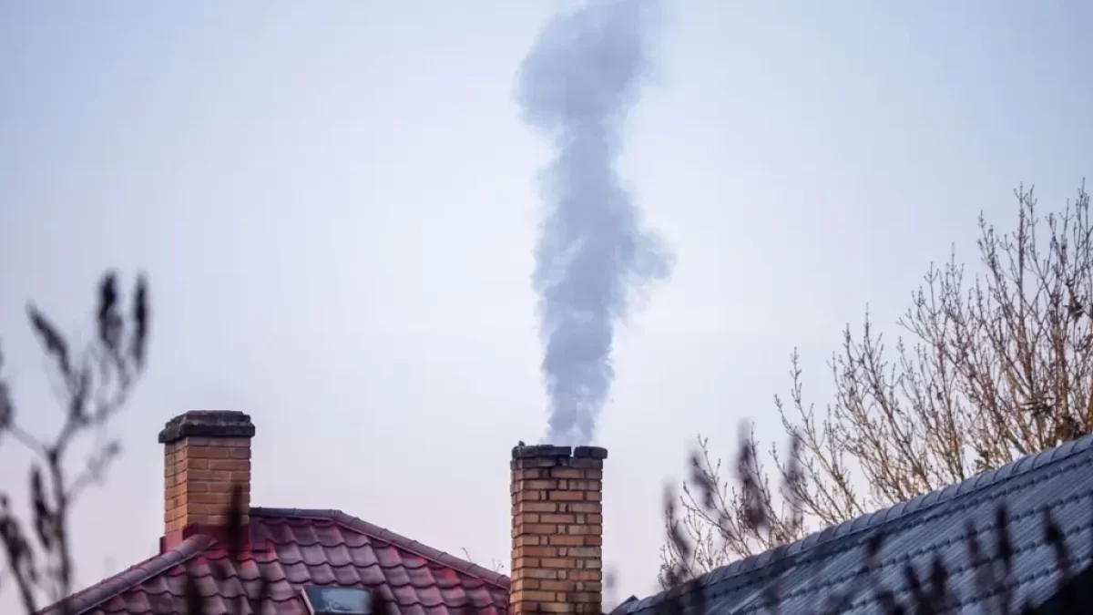 Čoudící komín rodinného domu a záběr na zasněžené střechy