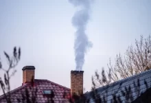 Čoudící komín rodinného domu a záběr na zasněžené střechy