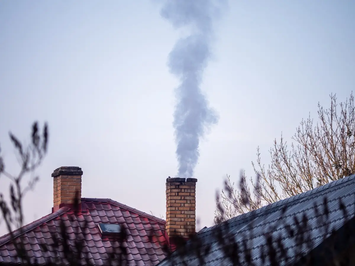 Čoudící komín rodinného domu a záběr na zasněžené střechy