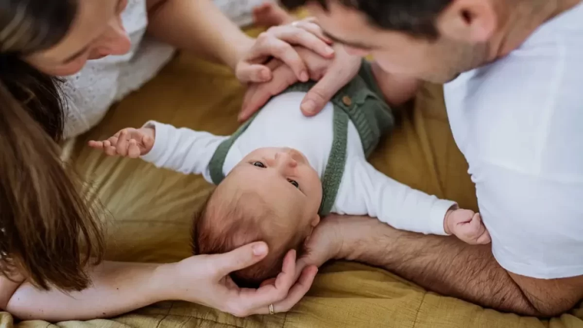 Rodiče leží na sedačce a sledují láskyplně své miminko, které je mezi nimi