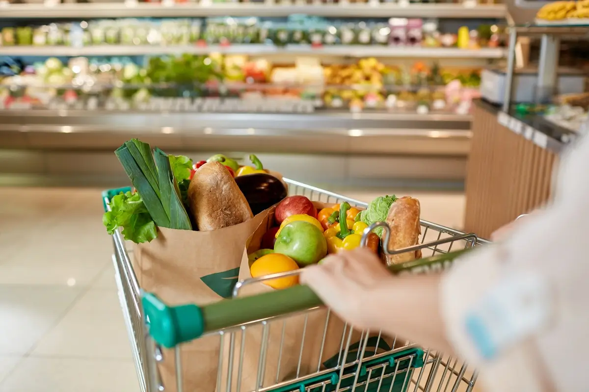 Ruce člověka tlačící plný nákupní vozík v supermarketu