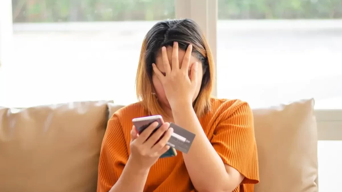 Mladá žena s telefonem a bankovní kartou se drží za hlavu