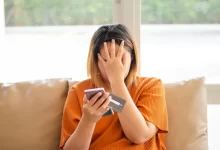 Mladá žena s telefonem a bankovní kartou se drží za hlavu