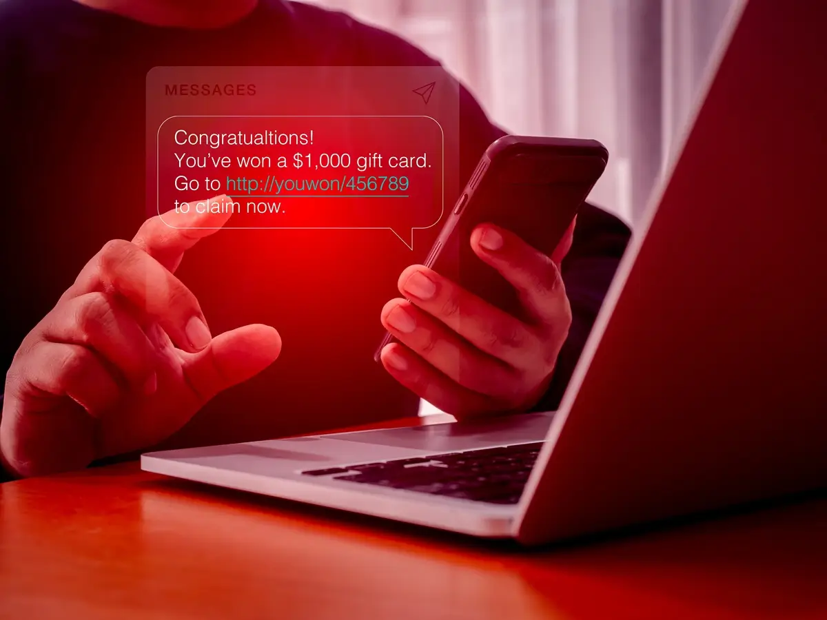 Phishing 2 - SportDeník Mužské ruce s mobilním telefonem v ruce, před nimi notebook a v éteru podvodná zpráva s gratulací k výhře