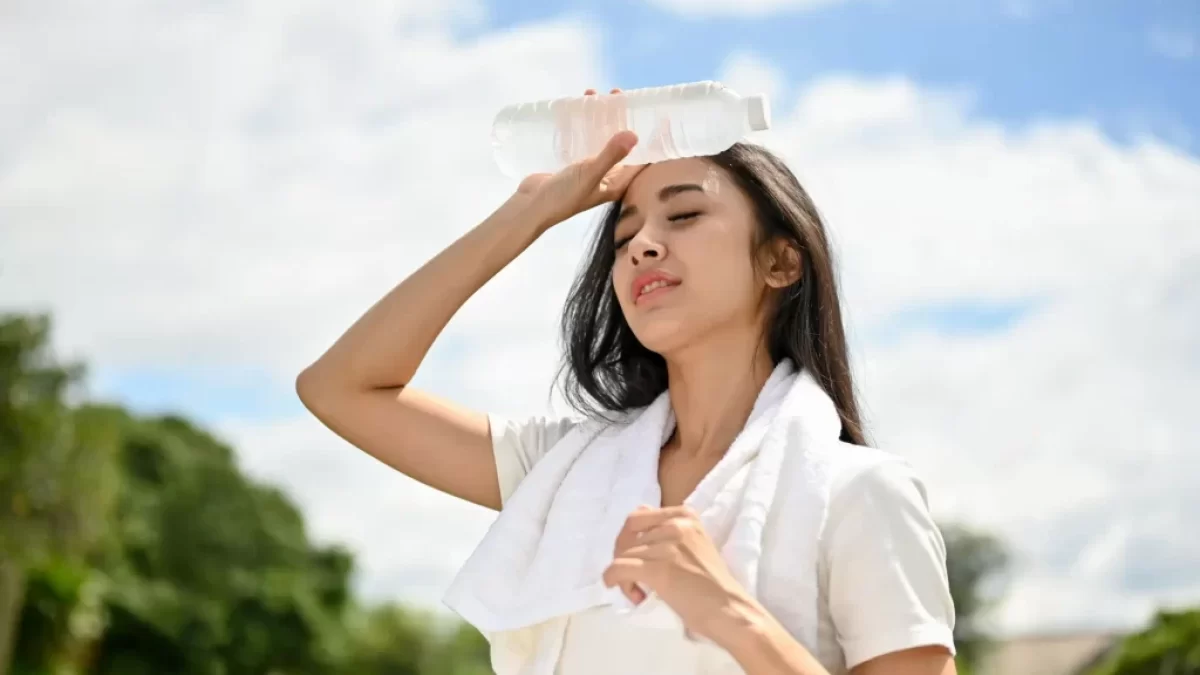 Žena chladící si čelo studenou lahví v horkém počasí