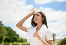 Žena chladící si čelo studenou lahví v horkém počasí