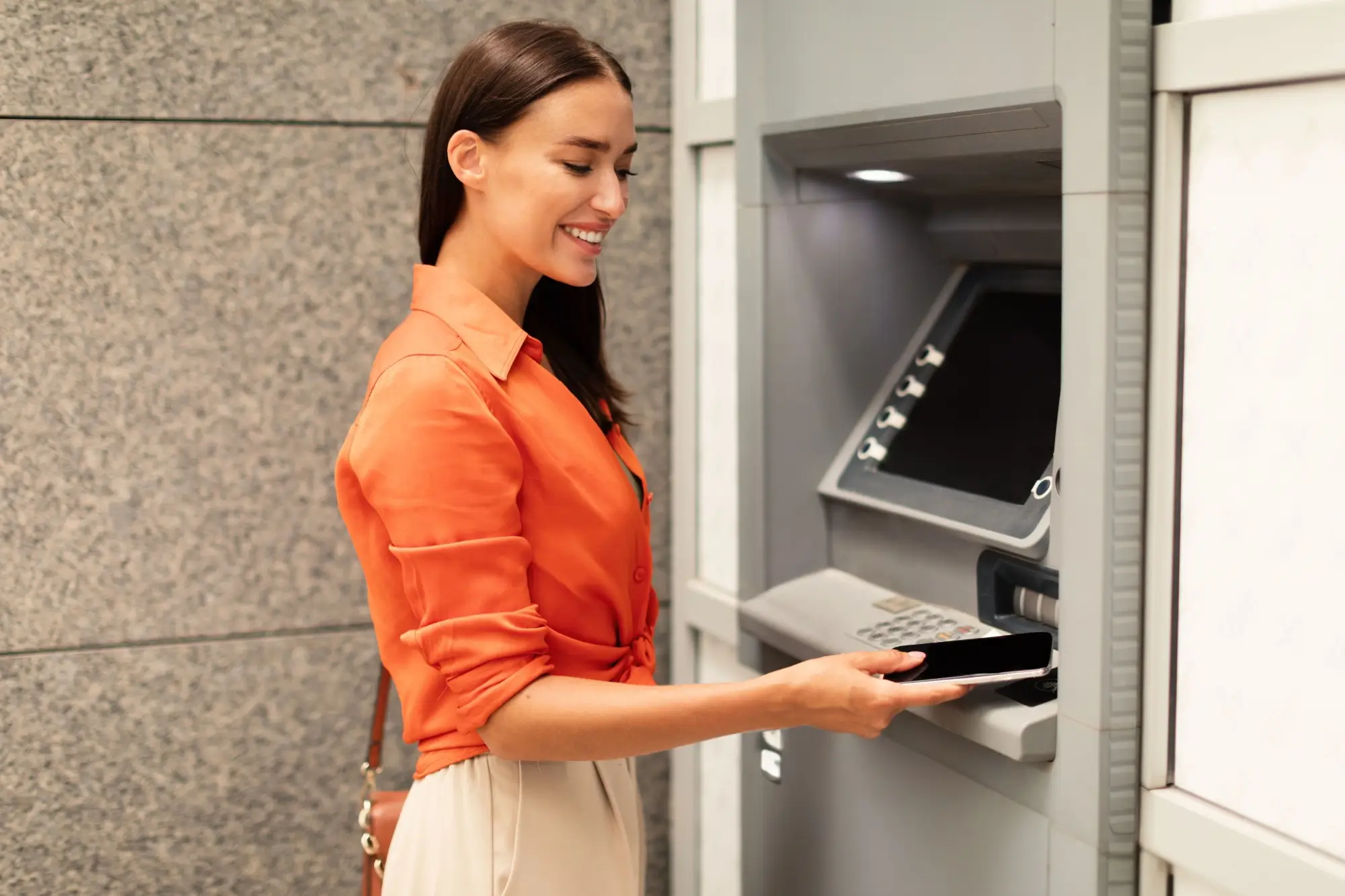Shutterstock_2359624077 - SportDeník Žena vybírající z bankomatu za pomoci mobilu