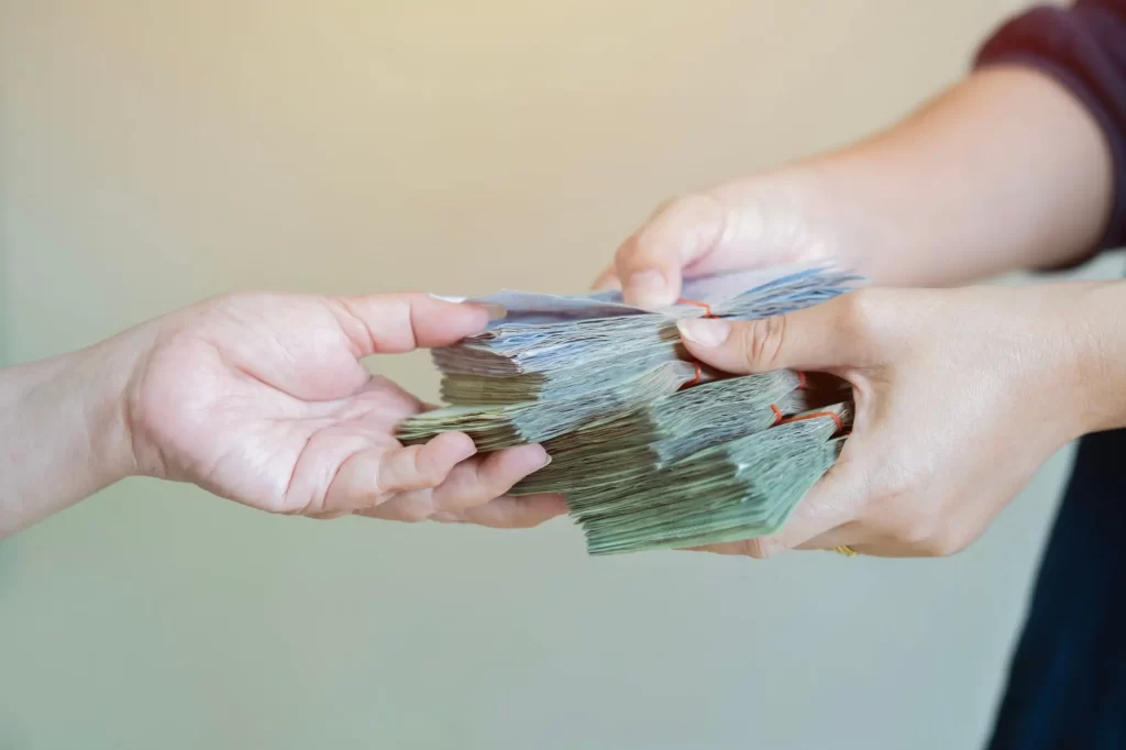 Shutterstock_2409418915 - SportDeník Ruce předávající si balík bankovek