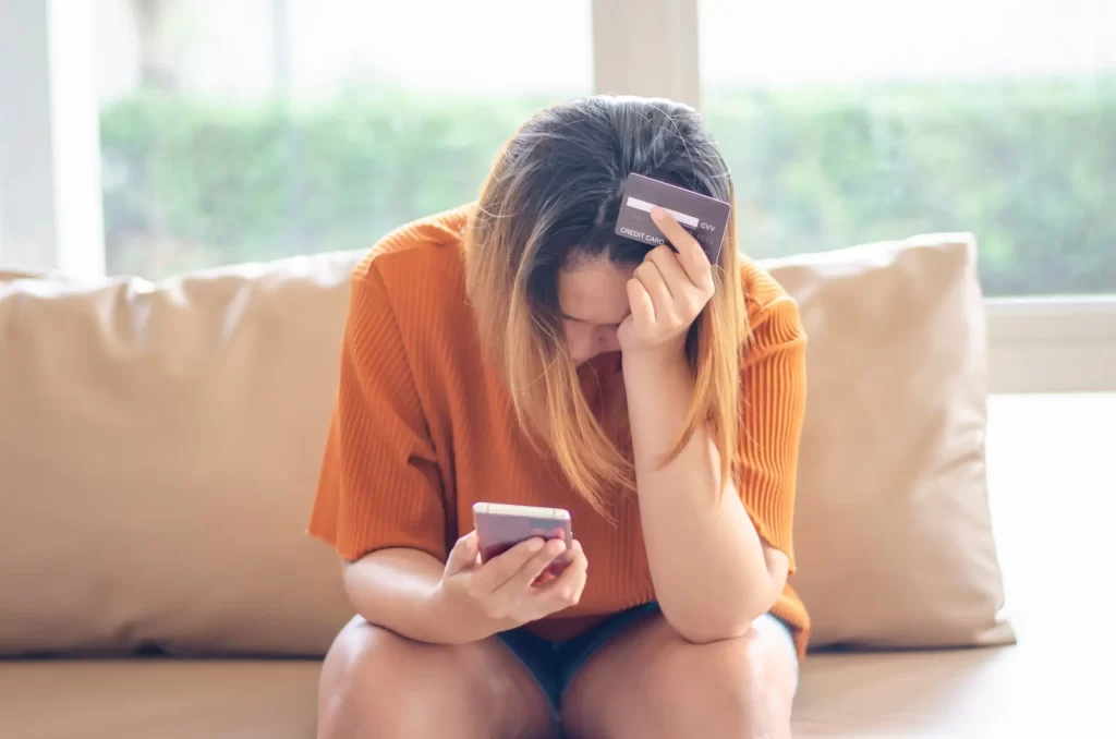 Nešťastná žena na gauči držící v ruce telefon a platební kartu