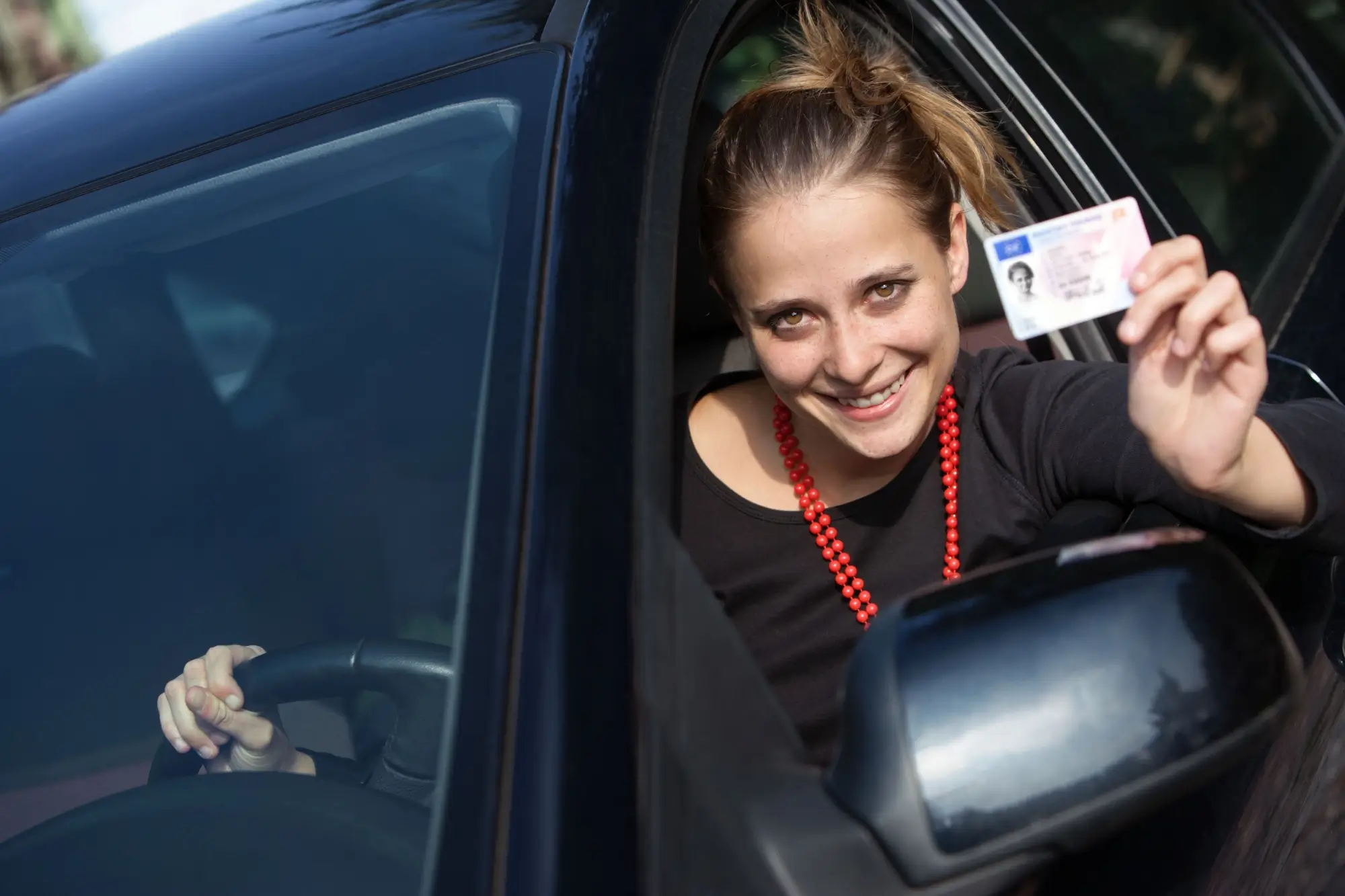 Žena za volantem ukazuje řidičský průkaz
