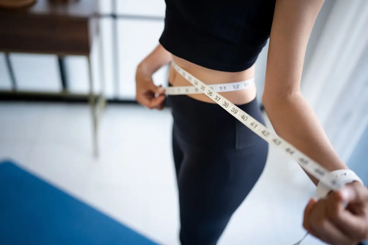 Mladá žena ve sportovním oblečení si měří centimetry v pase