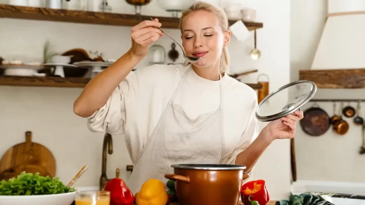Mladá žena ochutnává polévku z hrnce ve své kuchyni