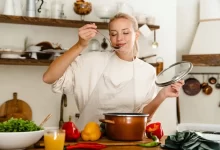 Mladá žena ochutnává polévku z hrnce ve své kuchyni