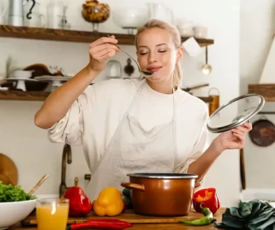 Mladá žena ochutnává polévku z hrnce ve své kuchyni