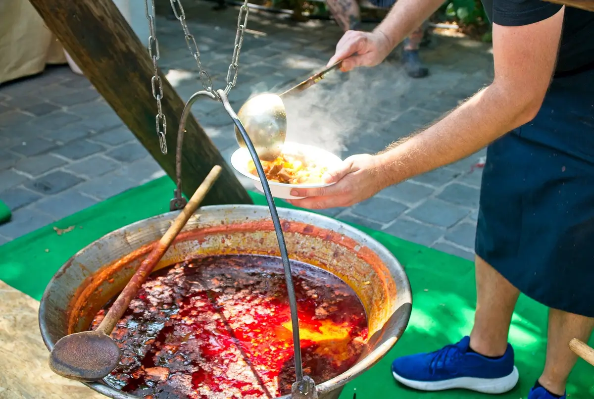 Muž v zástěře vaří kotlíkový guláš na ohni