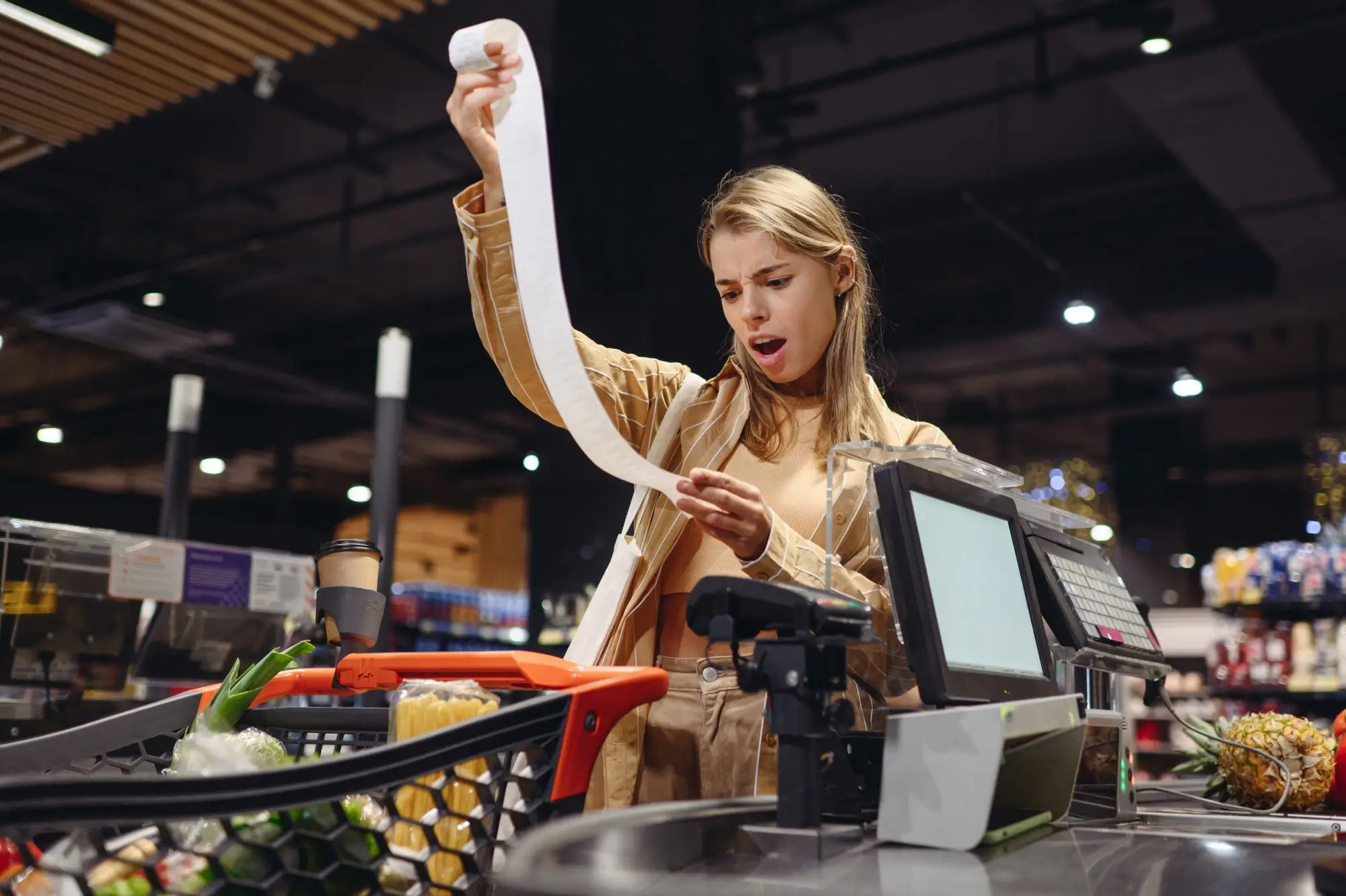 zděšená žena s účtenkou u pokladny v supermarketu