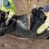 Dva muži ve žlutých reflexních vestách sází stromek do geotextilie
