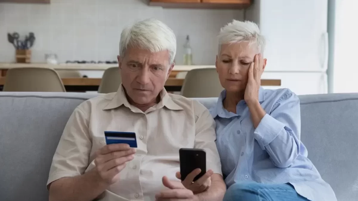 Starší manželský pár hledí nevěřícně na svou platební kartu a do mobilního telefonu