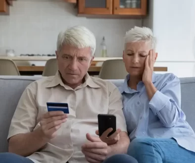 Starší manželský pár hledí nevěřícně na svou platební kartu a do mobilního telefonu