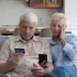 Starší manželský pár hledí nevěřícně na svou platební kartu a do mobilního telefonu