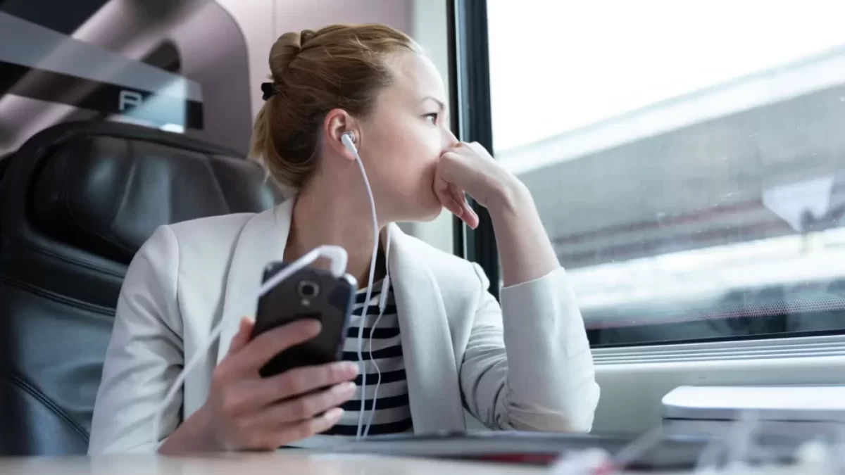 Žena s mobile v ruce a nasazenými sluchátky sedící ve vlaku