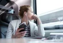 Žena s mobile v ruce a nasazenými sluchátky sedící ve vlaku