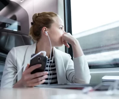 Žena s mobile v ruce a nasazenými sluchátky sedící ve vlaku