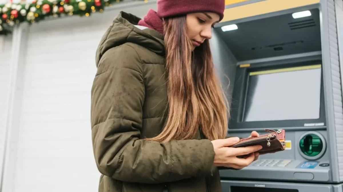 Dívka používající mobil u bankomatu