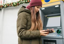 Dívka používající mobil u bankomatu