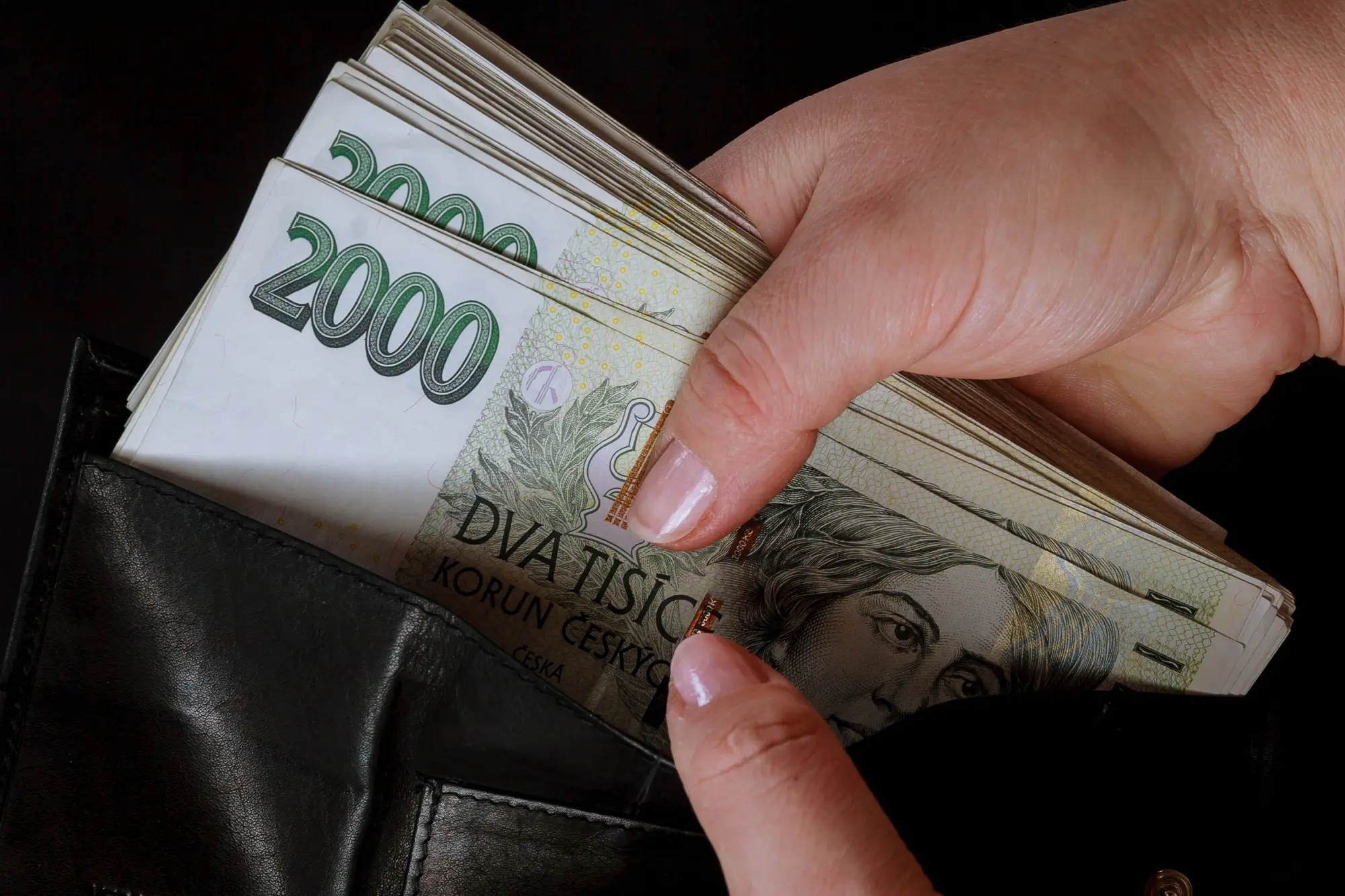 Ruka vyndávající dvoutisícové bankovky z peněženky