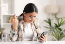 Žena sleduje mobil a gestikuluje, ilustruje frustraci z nefunkční bankovní aplikace
