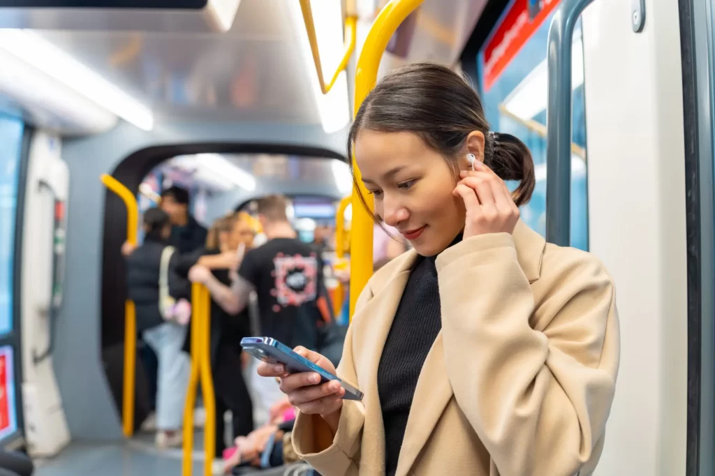 Shutterstock_2410356071 - SportDeník Mladá žena se sluchátky v uších a mobilem v ruce stojící v tramvaji