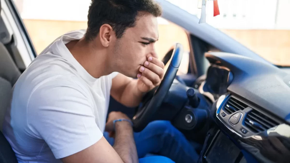 Mladý muž v autě držící si ústa a nos kvůli zápachu