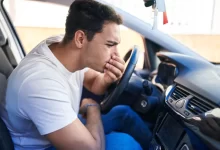 Mladý muž v autě držící si ústa a nos kvůli zápachu