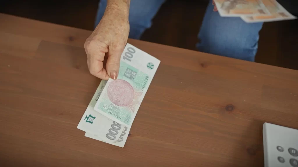 - SportDeník Důchodkyně drží peníze, symbol očekávaného zvýšení důchodů.