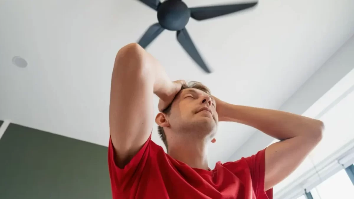 Muž ve stresu z horka pod stropním ventilátorem.