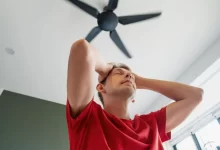 Muž ve stresu z horka pod stropním ventilátorem.