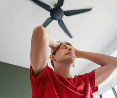 Muž ve stresu z horka pod stropním ventilátorem.
