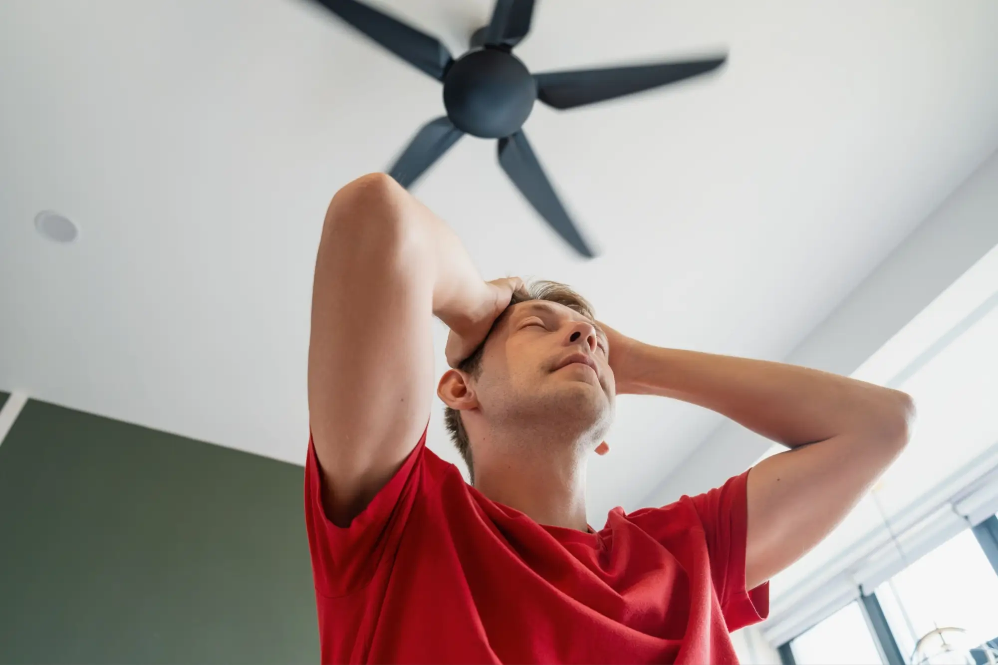 Muž ve stresu z horka pod stropním ventilátorem.