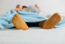 Osoba ležící pod modrou přikrývkou s oranžovými ponožkami.