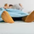 Osoba ležící pod modrou přikrývkou s oranžovými ponožkami.