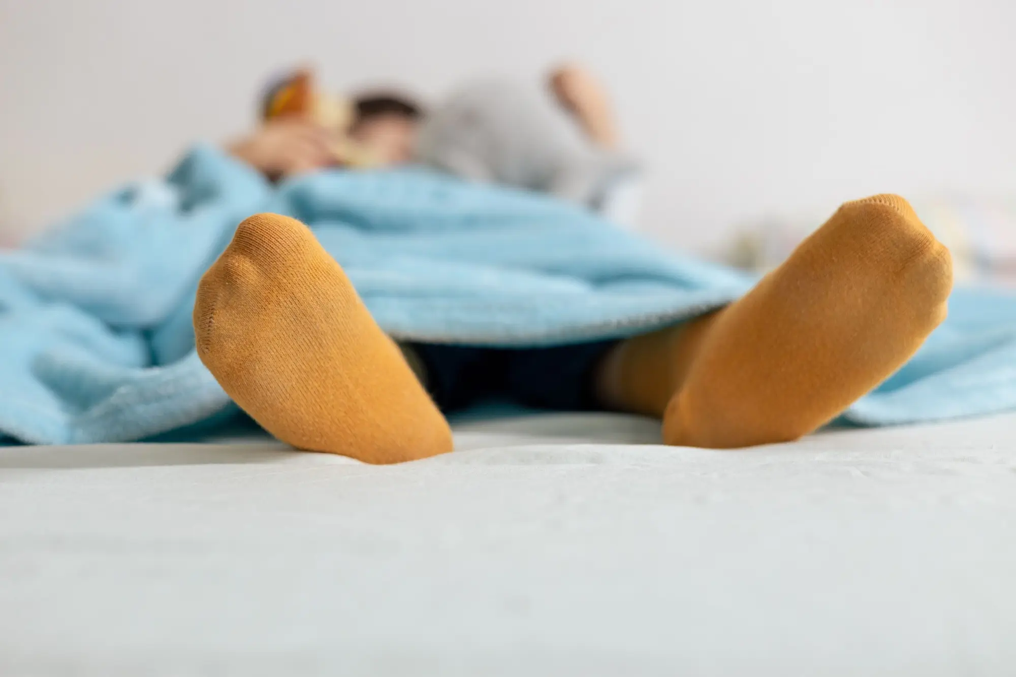 Osoba ležící pod modrou přikrývkou s oranžovými ponožkami.