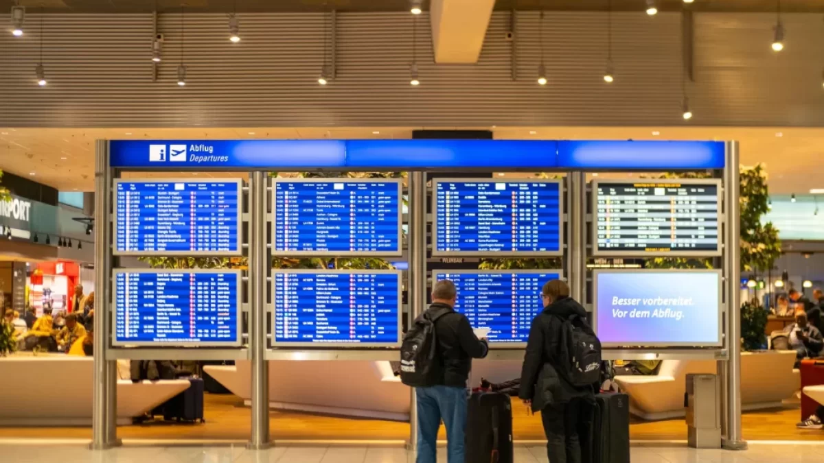 Cestující čekající na letišti před cedulí s odlety