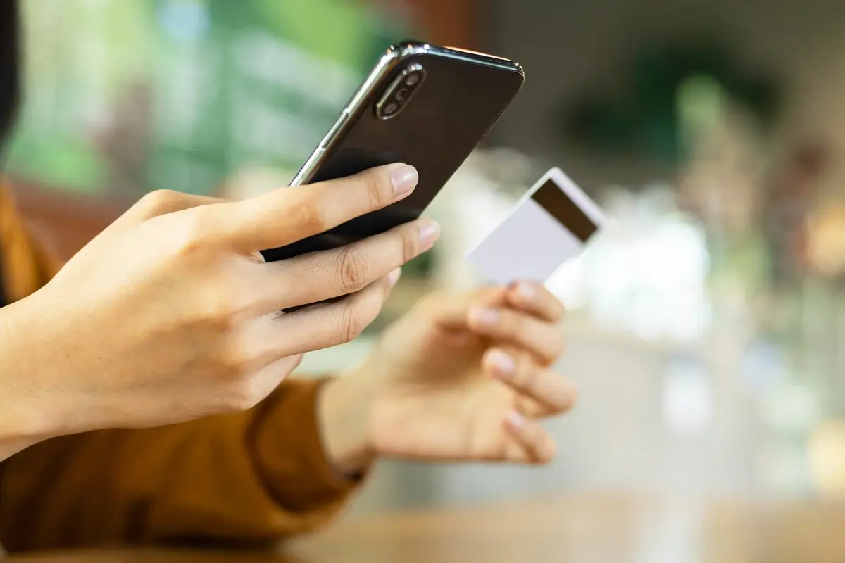 VZP 2 - SportDeník Ženské ruce drží platební kartu a kontrolují mobilní telefon
