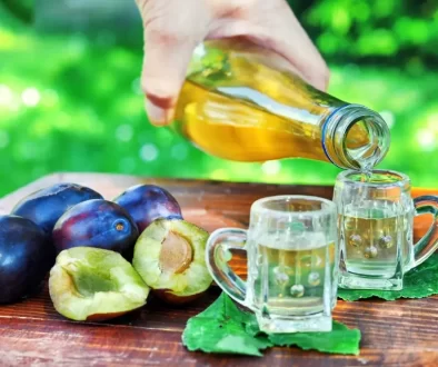 Mužská ruka nalévá do dvou štamprlí domácí slivovici, na stole jsou rozsypané zralé trnky